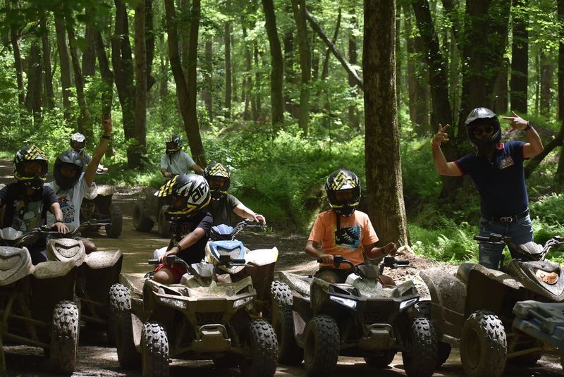 Big group of riders lined up on ATVs in the woods, waving at the camera